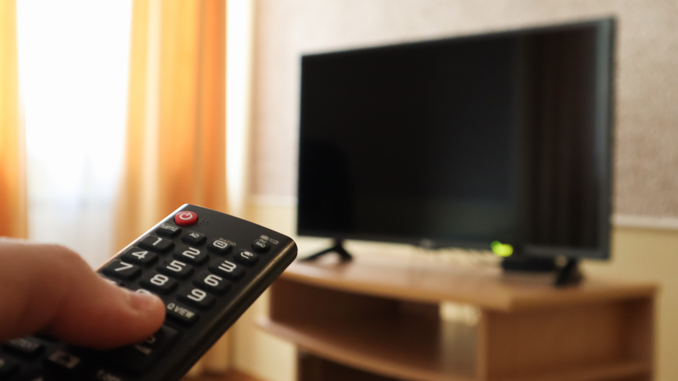 hotel entertainment systems. Hand holding a television remote control and surfing programs on television. watch, turn on or off the TV in the living room or bedroom on the black-screen nightstand. Copy space