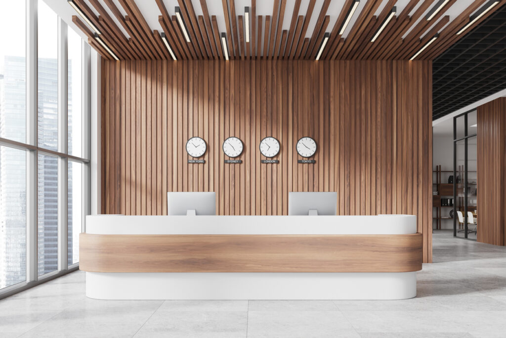 An empty but very modern looking hotel lobby. Four clocks for different locations are on the wall above the empty check-in desk.