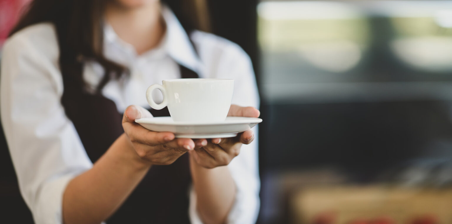 Close-up of beautiful young female waitress serving a cup of coffee to customers in cafe