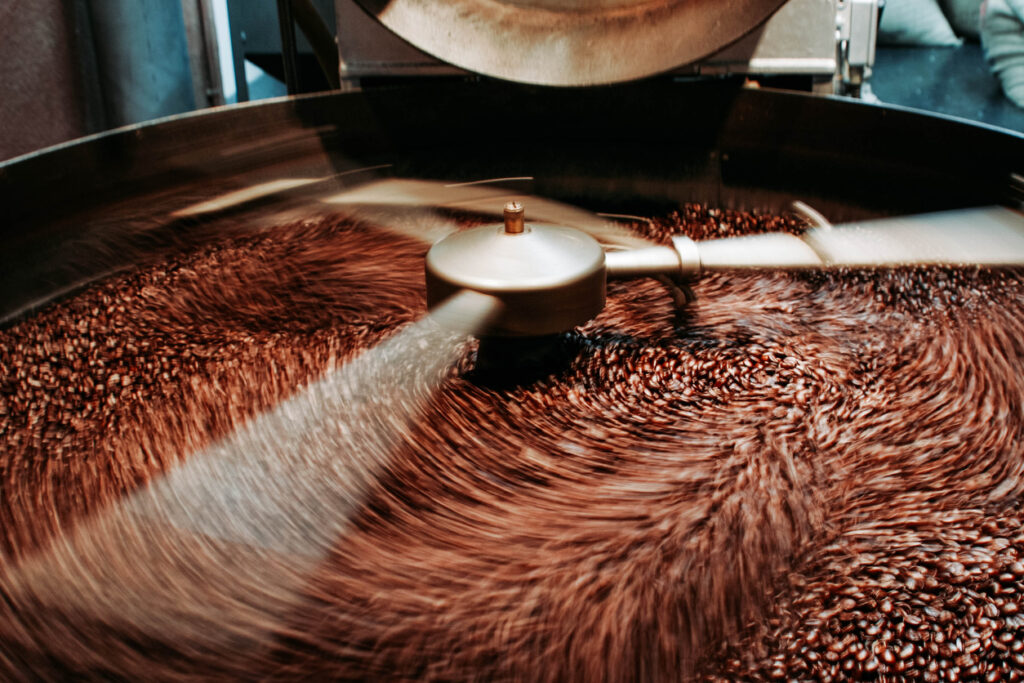 A close up photo of a coffee roaster that is spinning gently roasting a lot of new coffee beans. coffee price increases